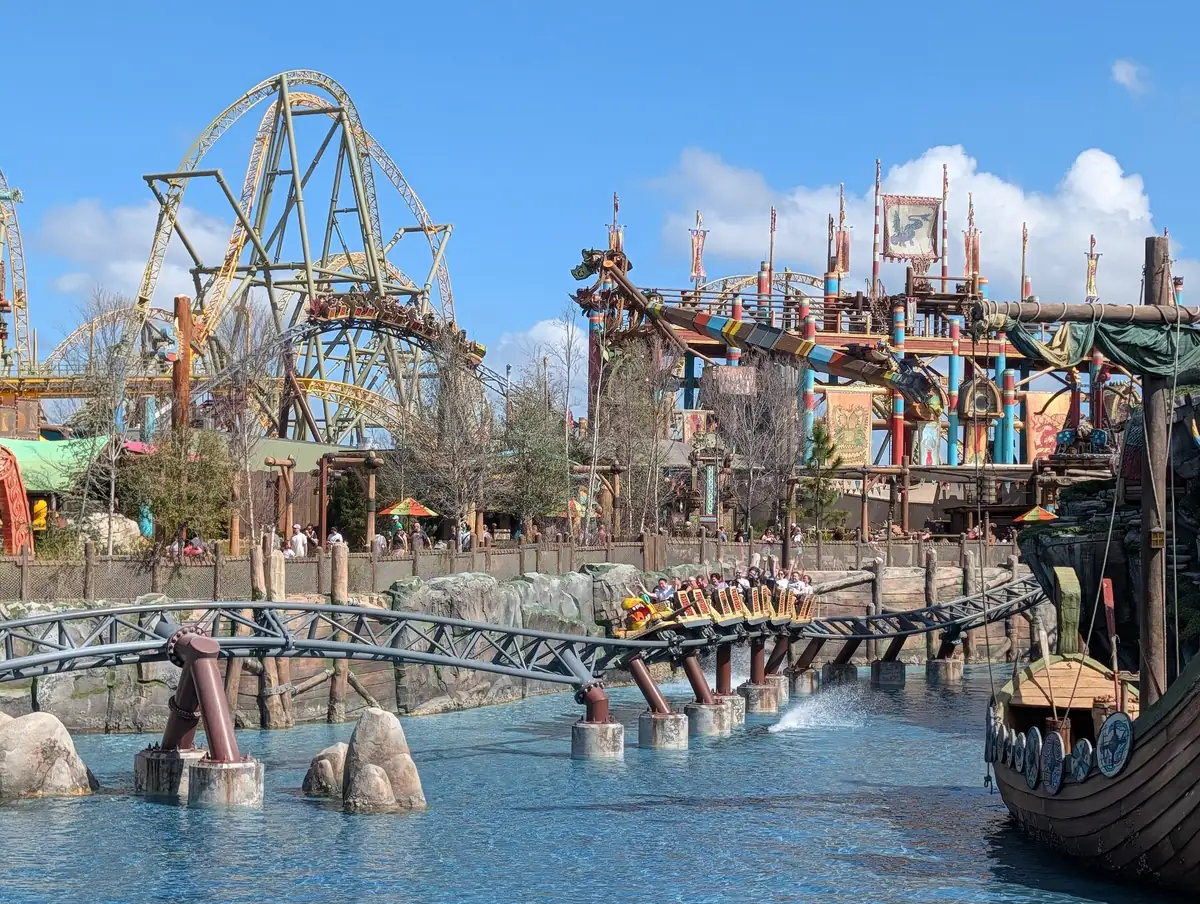 Hiccup's Wing Gliders coaster skimming the lake past a Viking ship in the Isle of Berk at Epic Universe