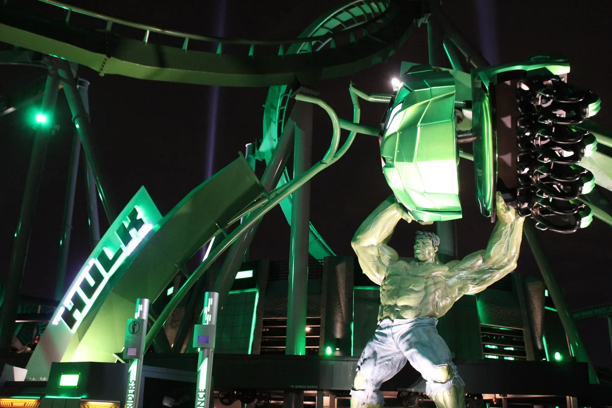 The Incredible Hulk Coaster entrance at night, a Hulk statue holding a ride car under green-lit track