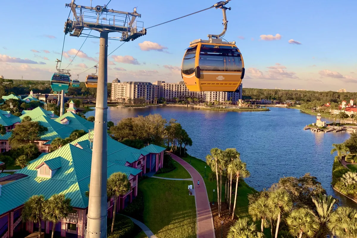 A Disney Skyliner gondola on its cable above Caribbean Beach Resort's lake and rooftops
