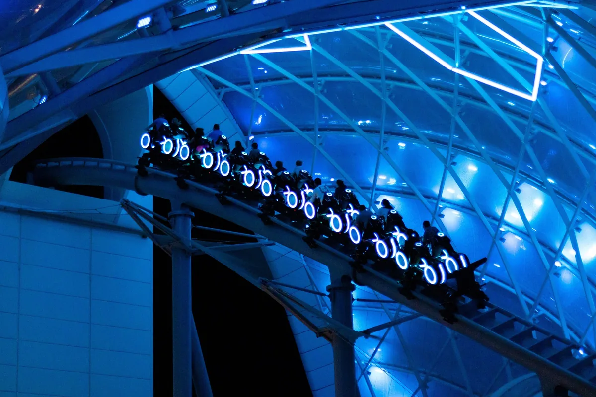 TRON Lightcycle / Run train racing under its glowing blue canopy at night at Magic Kingdom