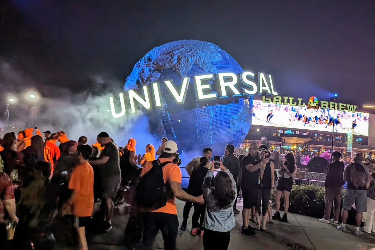The Universal globe lit up blue at night in fog, with guests gathered around it at Universal Orlando