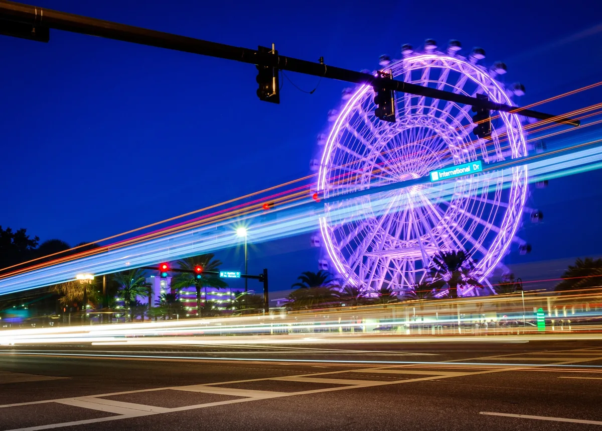 Traffic light trails on International Drive at dusk with the purple-lit Orlando Eye wheel behind