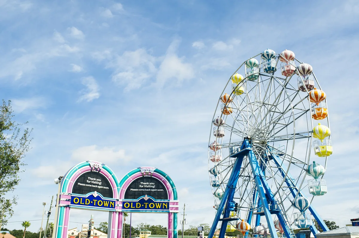 Old Town Kissimmee's jukebox-style entrance signs and colorful Ferris wheel under a blue sky