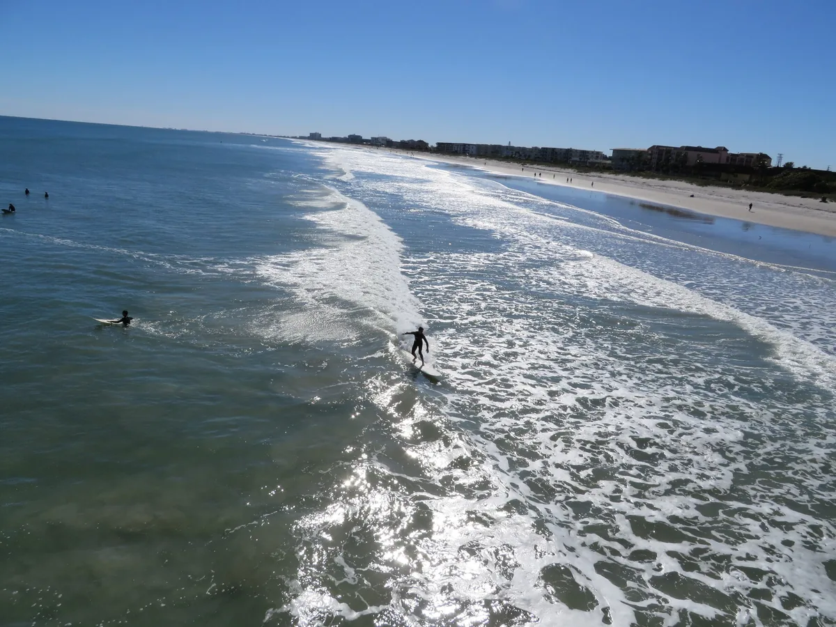 Surfers in the breakers below the Cocoa Beach Pier, with the long sandy beach beyond