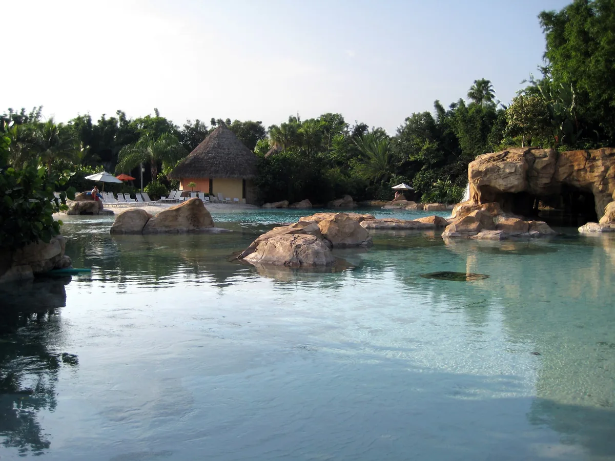 A calm lagoon at Discovery Cove ringed by rocks, palms and a thatched-roof hut