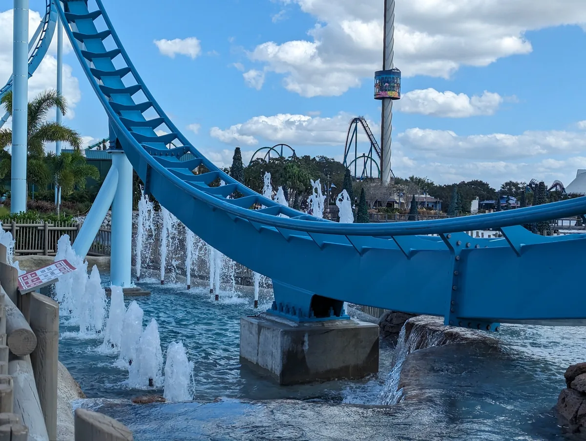 Pipeline: The Surf Coaster's blue track over splashing fountains, with SeaWorld's Sky Tower behind