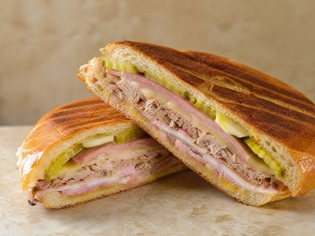 A pressed Cuban sandwich cut in half, showing ham, roast pork, Swiss cheese and pickles