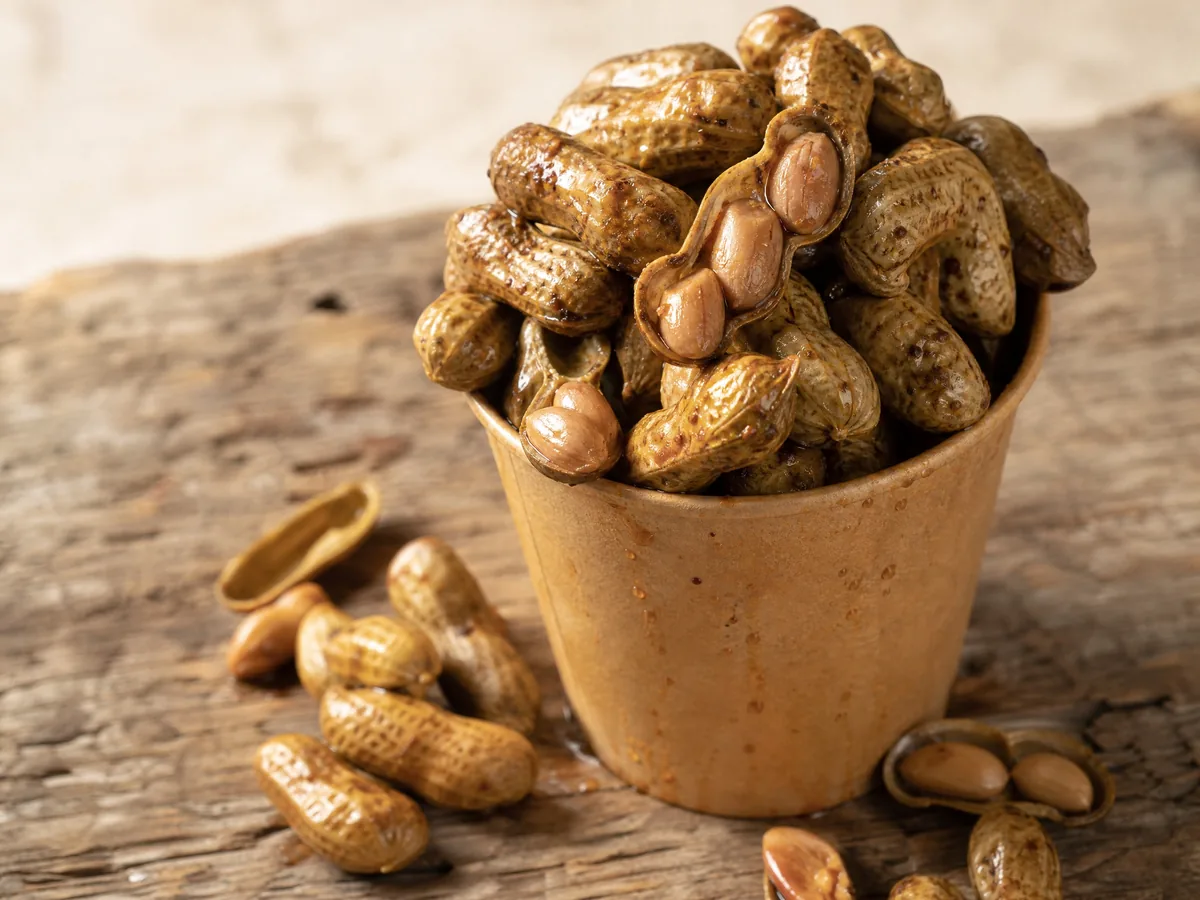 A paper cup of boiled peanuts in their shells on a wooden table
