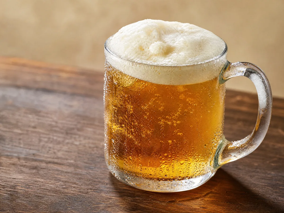A glass mug of amber butterscotch soda under a thick cream foam