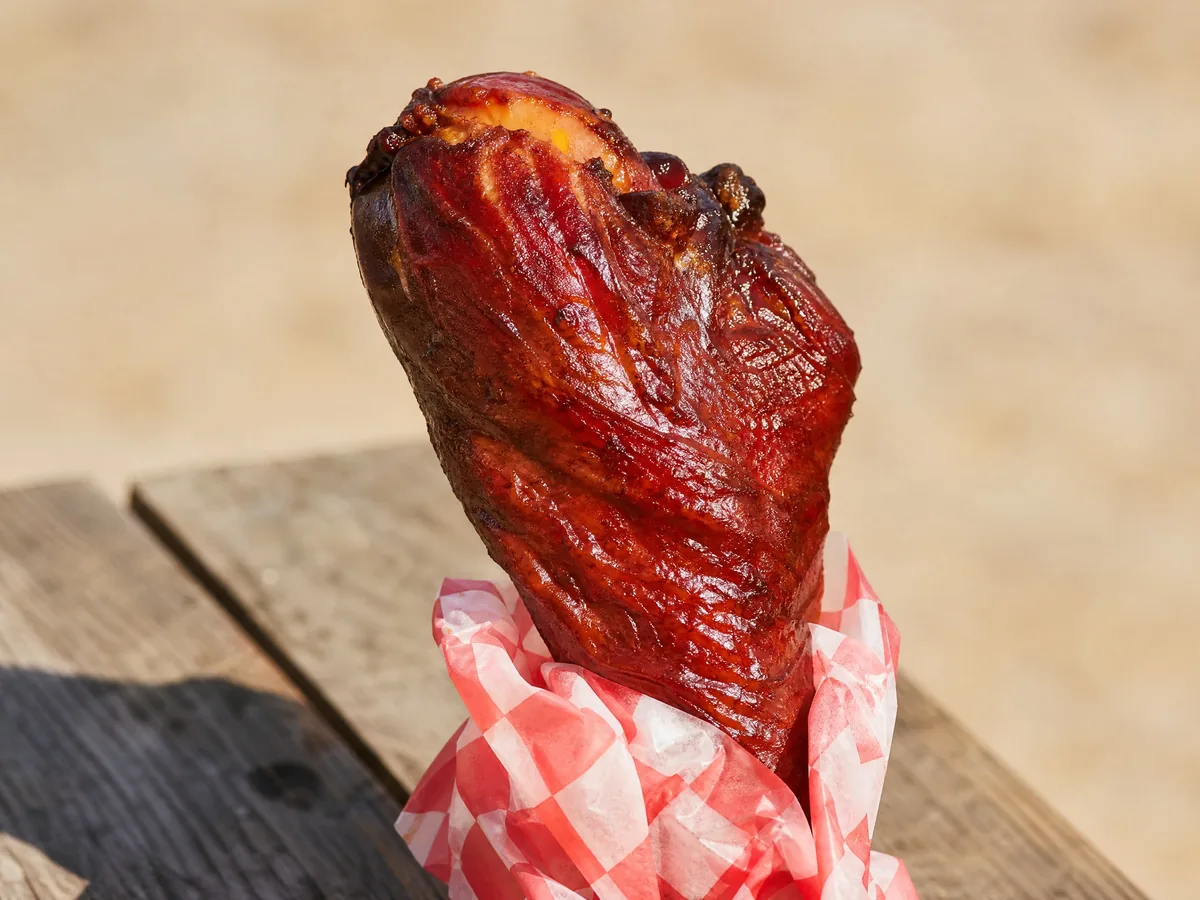 A dark, glossy smoked turkey leg wrapped in checked paper