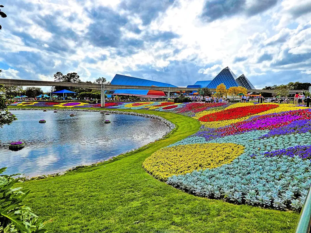 Swirling flower beds beside a pond with the Imagination pavilion's glass pyramids behind at EPCOT