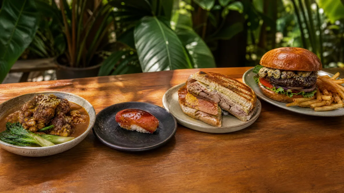 Four plates side by side: oxtail peanut stew, a piece of nigiri, a Cuban sandwich and a blue cheese burger