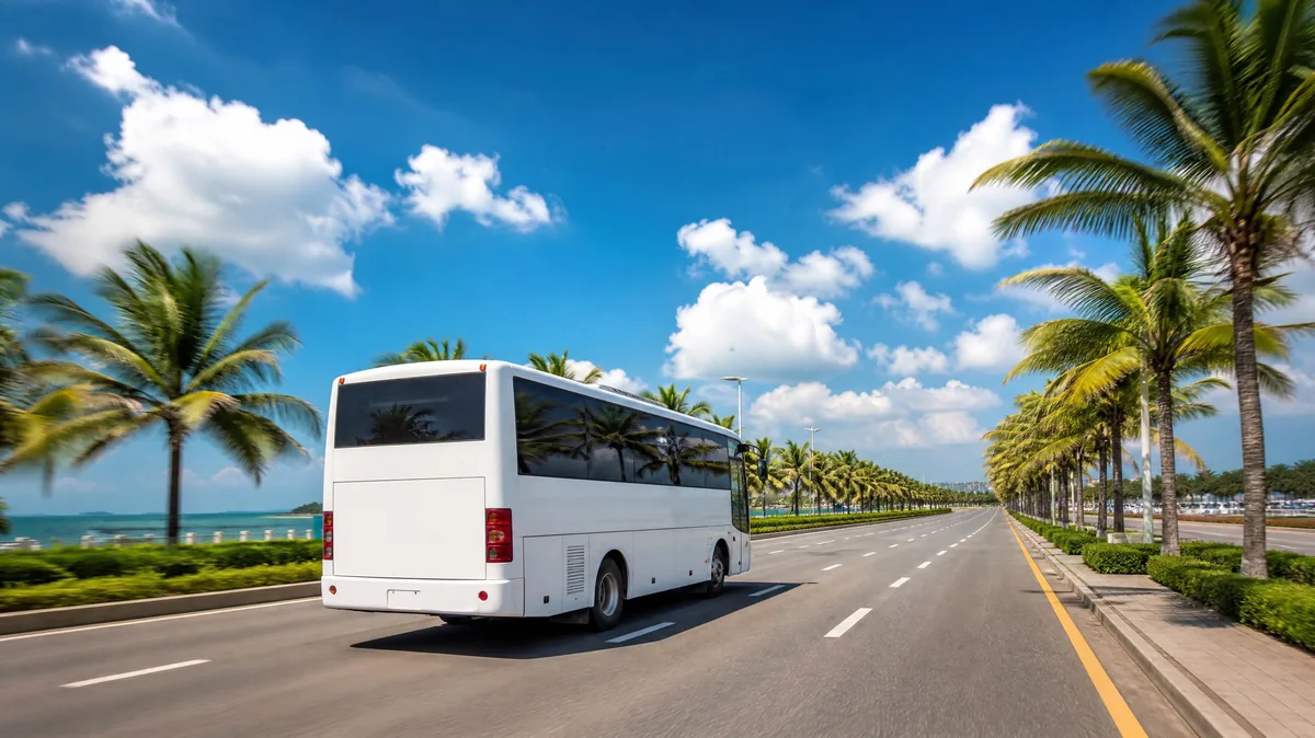 A plain white shuttle bus on a palm-lined road under a blue sky