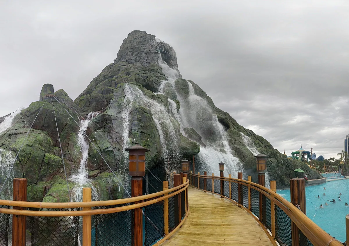 Krakatau volcano with waterfalls at Volcano Bay, seen from a wooden boardwalk by the wave pool