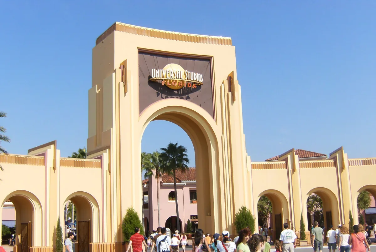 Guests passing through the arched main entrance gate of Universal Studios Florida on a sunny day