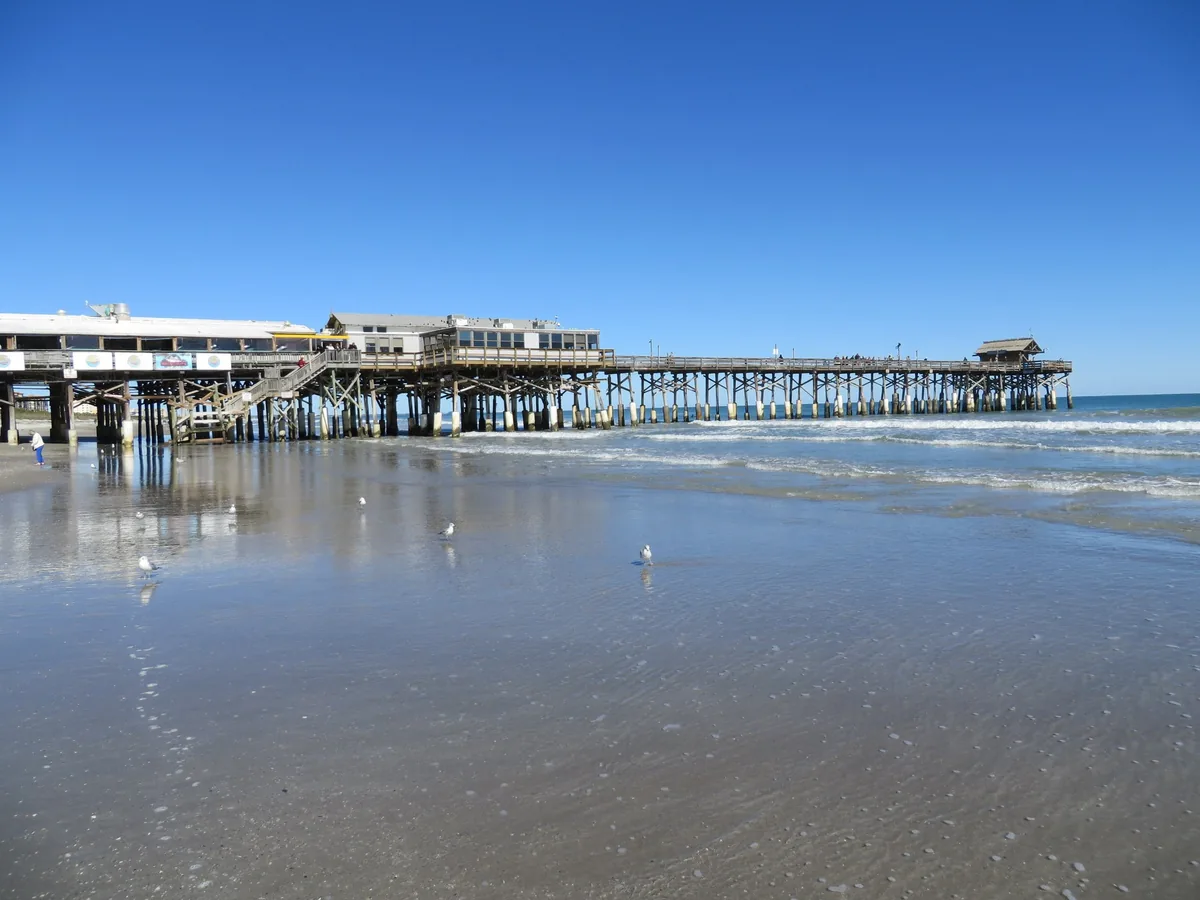 Cocoa Beach Pier reaching into the Atlantic over a wide, glassy beach under a clear sky