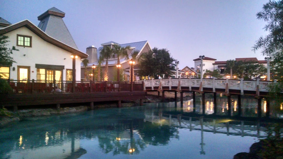 Disney Springs Town Center at dusk, with lamps reflected in the water beside a footbridge