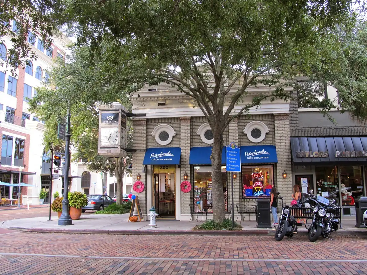 Brick-paved Park Avenue in Winter Park with a shade tree and boutiques under blue awnings